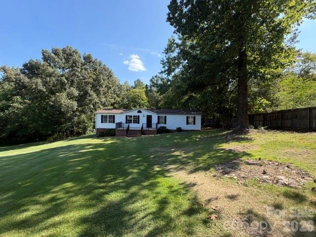 White single-story home beyond a sloping lawn, shaded by mature trees beside a wooden fence.