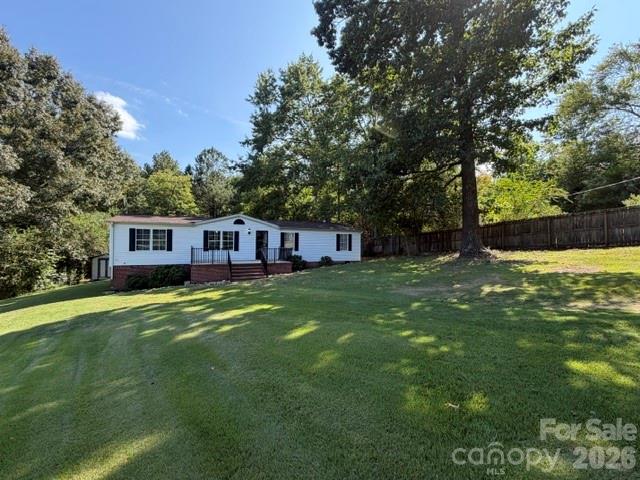 Single-story white home with a brick foundation sits beyond a broad lawn beneath mature trees.