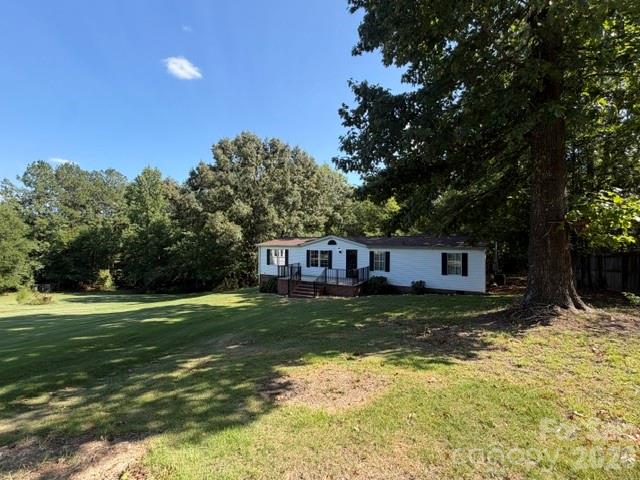 White single-story home with a raised porch beyond a broad lawn and mature trees.