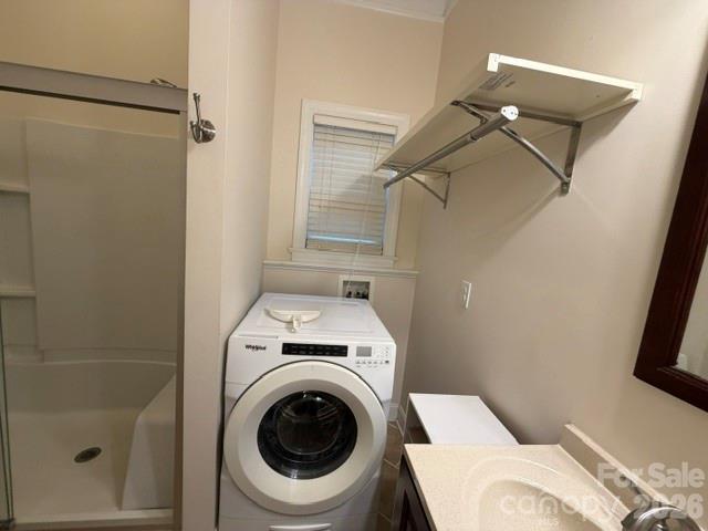 Laundry area with a front-loading washer, wall-mounted drying rack, and sink counter beside a shower.