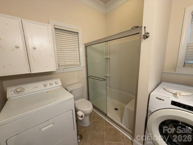 Laundry and bathroom with two washers, a toilet, and a glass-enclosed shower.