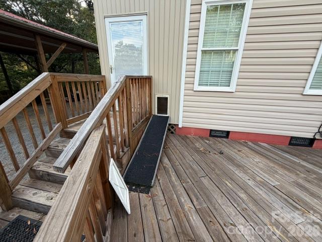 Wooden deck with stairs and a narrow ramp leading to a glass door on a beige-sided home.