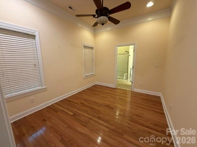 Empty bedroom with wood floors, a ceiling fan, and an open doorway to the bathroom.