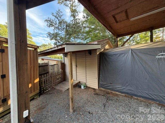 Covered gravel area with a small storage shed and tarp-covered shelter.