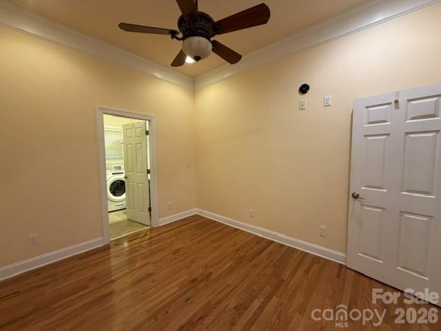 Empty room with hardwood floors and a ceiling fan, opening to a laundry area.