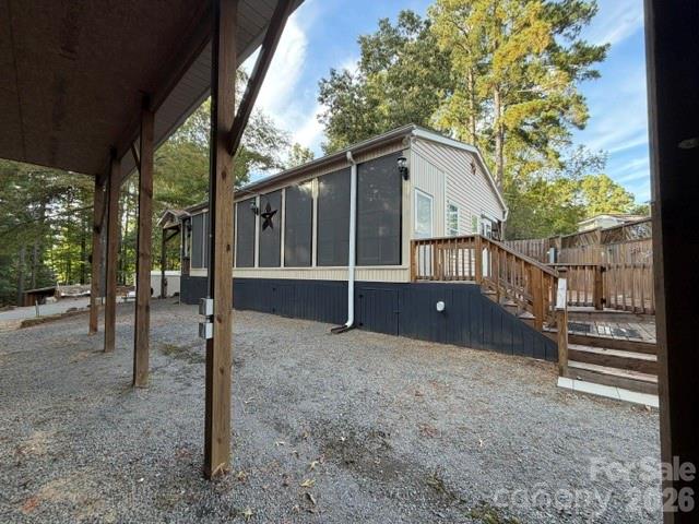 Manufactured home with a screened porch and raised wooden deck on a gravel lot.