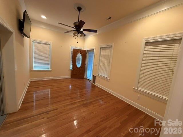 Vacant living room with glossy hardwood floors, multiple windows, and a ceiling fan.
