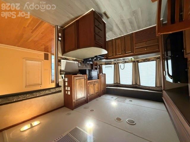 Kitchen with dark wood cabinetry, a central peninsula, and gray flooring beside a hardwood-floored room.