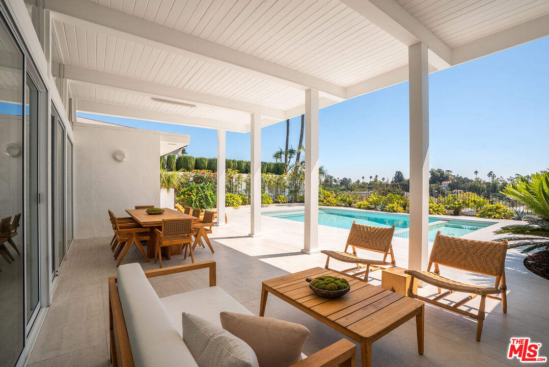 Covered patio with outdoor dining and lounge seating beside a swimming pool.