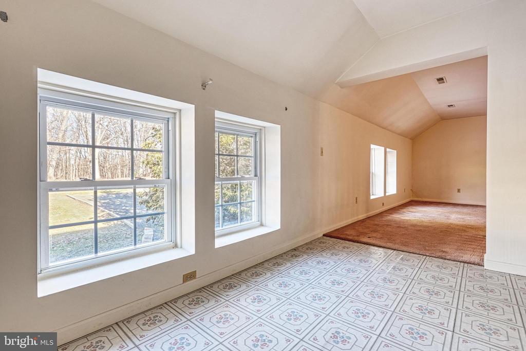 Empty room with large windows, patterned tile flooring, carpeted area, and a vaulted ceiling.