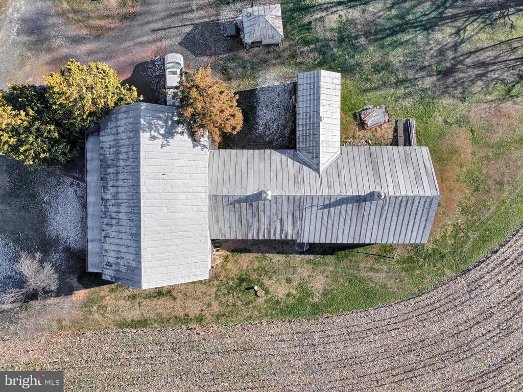 Aerial view of a rural property with a long metal-roofed building beside fields and a gravel drive.