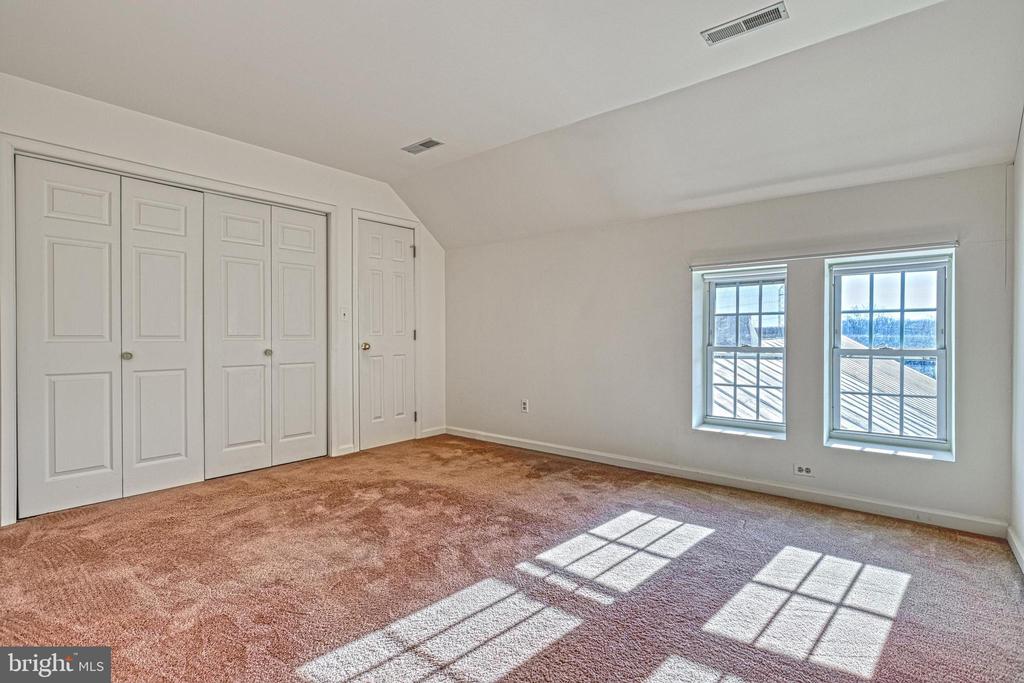 Vacant bedroom with paneled closets, two windows, and sunlight across the carpet.