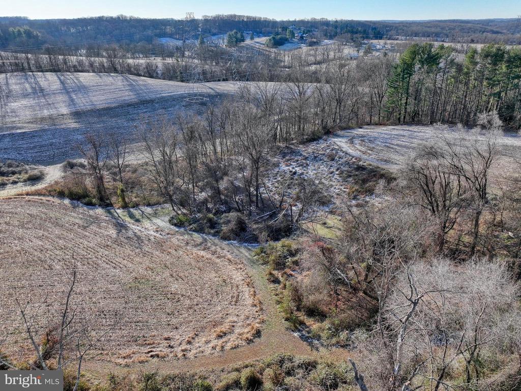 Aerial view of frosty fields and a wooded ravine across rural property.