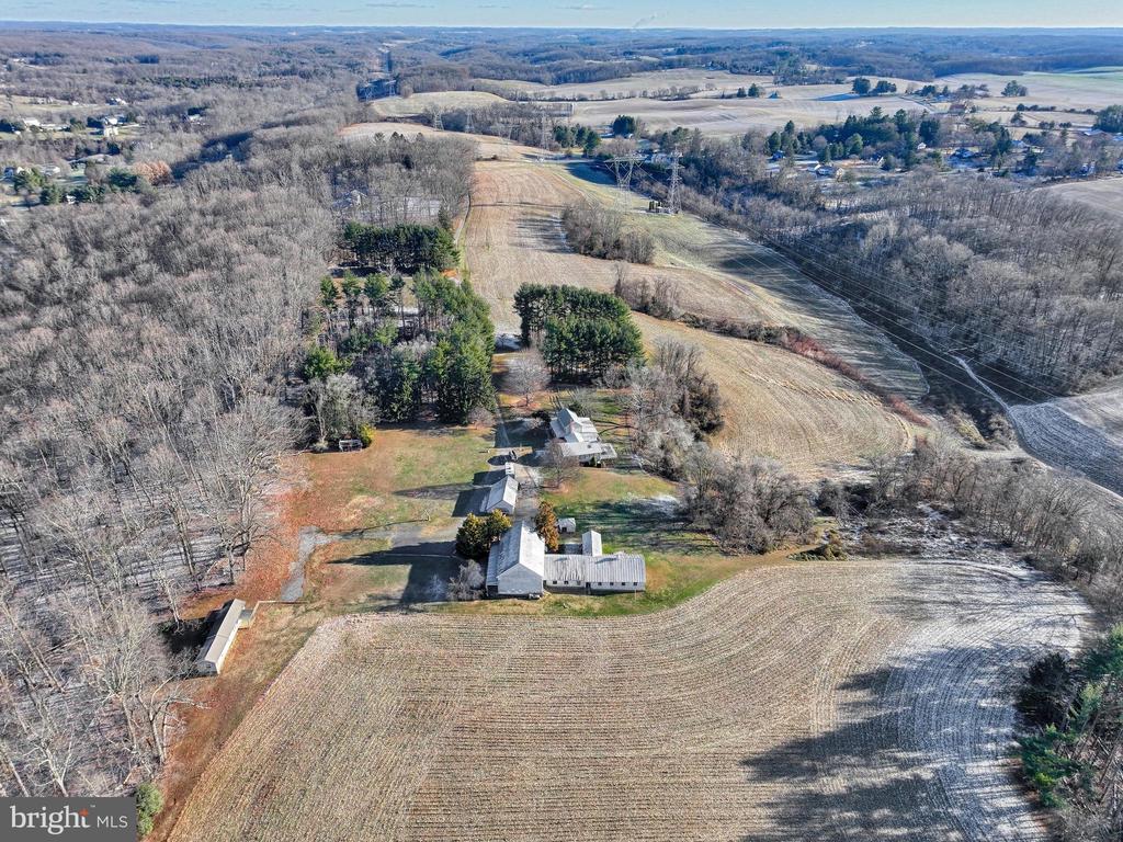 Rural property with several buildings among open fields and leafless woods, seen from above.