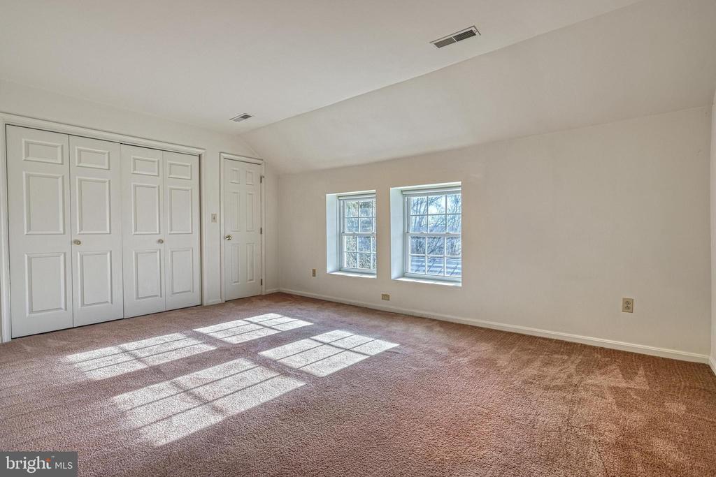 Empty carpeted bedroom with paneled closet doors and two sunlit windows.