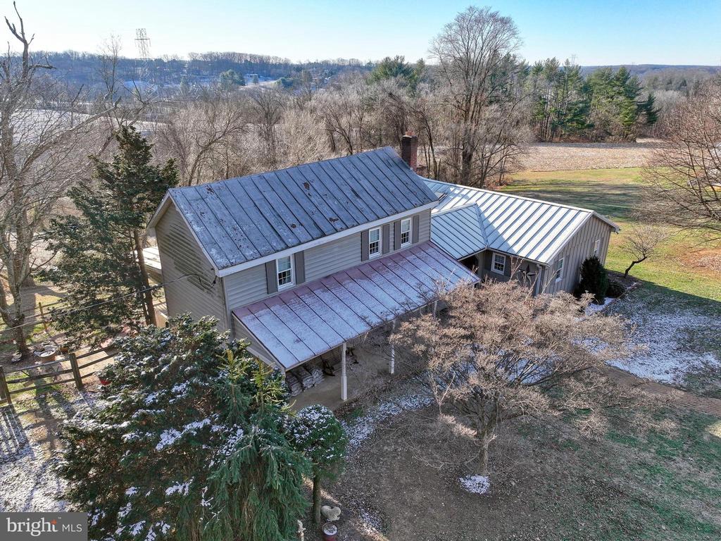 Aerial view of a rural home with multiple metal roofs, leafless trees, and open fields.