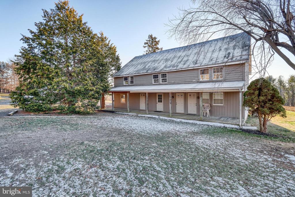 Gray two-story house with a metal roof and long covered porch beside a lightly snow-dusted lawn.