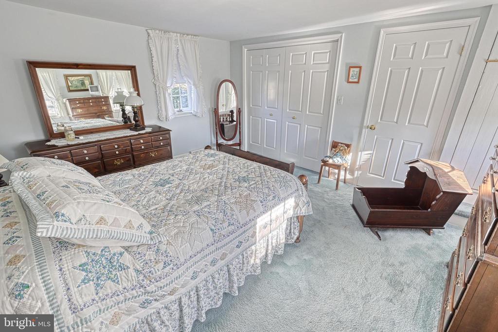 Bedroom with a patterned quilted bed, dark wood dresser and mirror, and white closet doors.