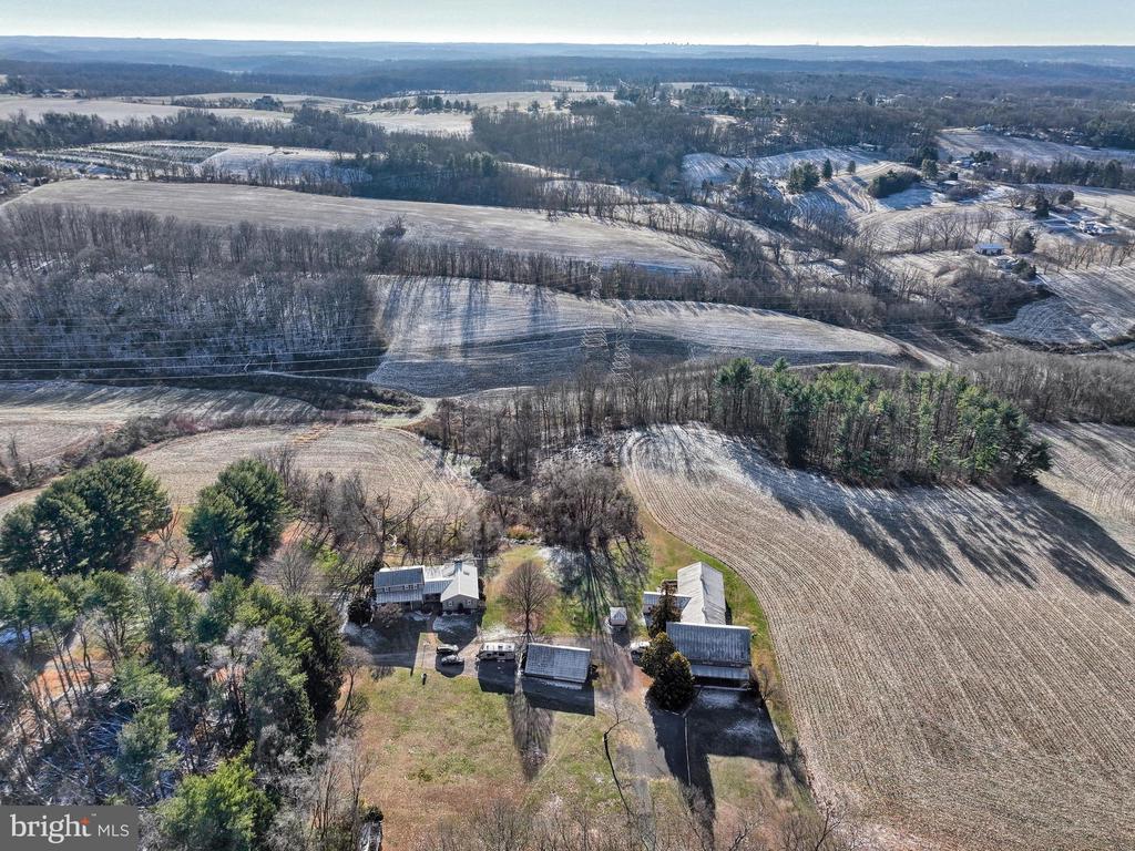 Aerial view of a rural property with several outbuildings beside expansive fields and woods.
