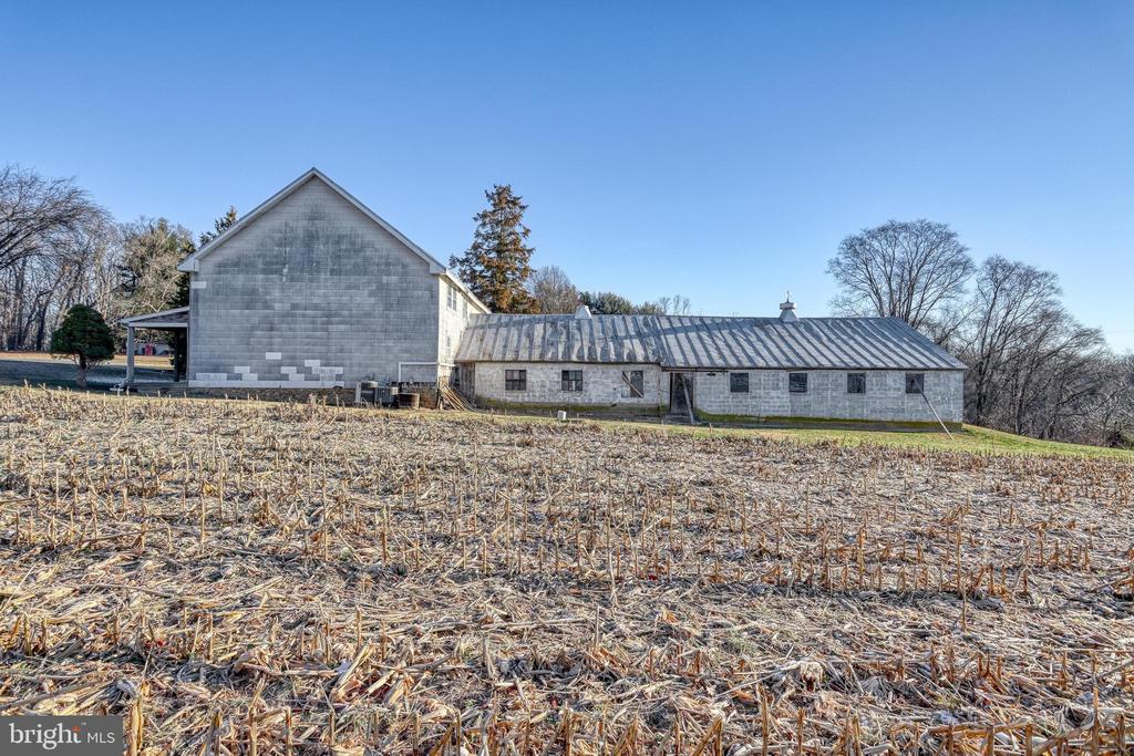 Rural property with a large gray gabled building, long stone outbuilding, and harvested field.
