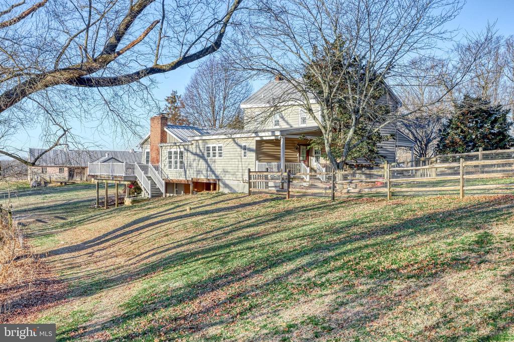 Rear of a light-colored house with a covered porch, deck and fenced sloping lawn.