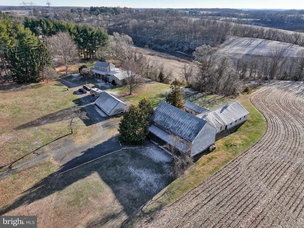 Aerial view of a rural farmhouse and outbuildings beside cultivated fields and woodland.