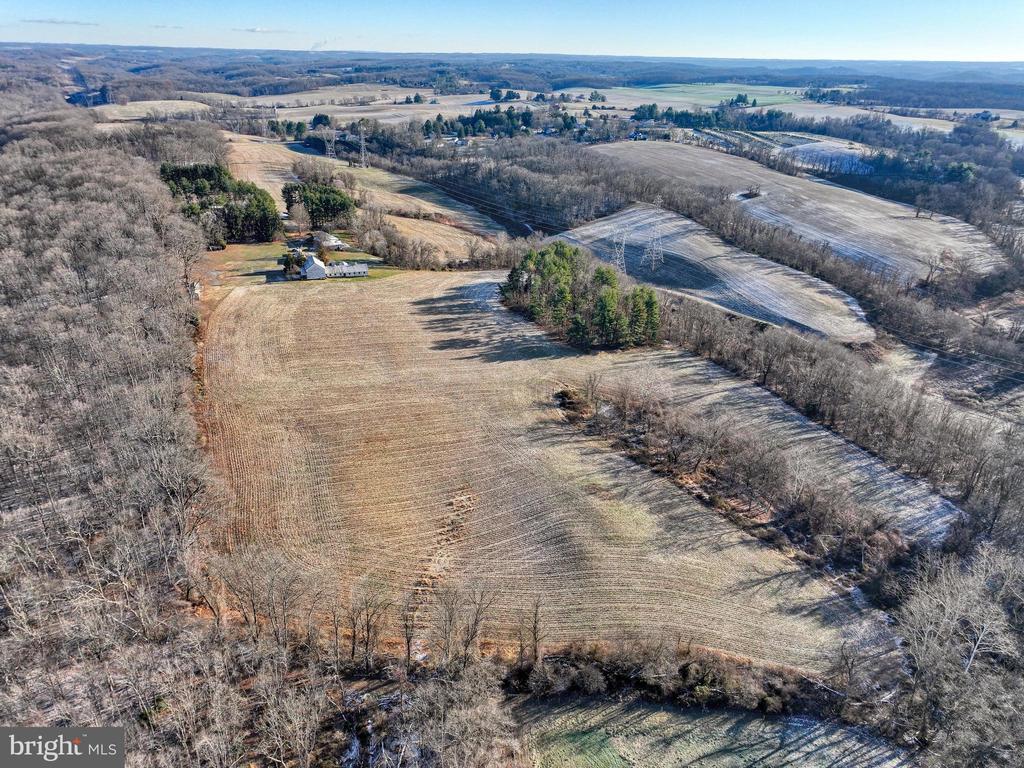 Aerial view of a rural property with a farmhouse, outbuildings, open fields, and surrounding woodland.