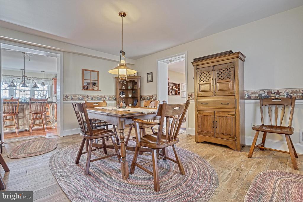 Dining room with a wooden table, braided rugs, and a tall hutch beside the kitchen doorway.