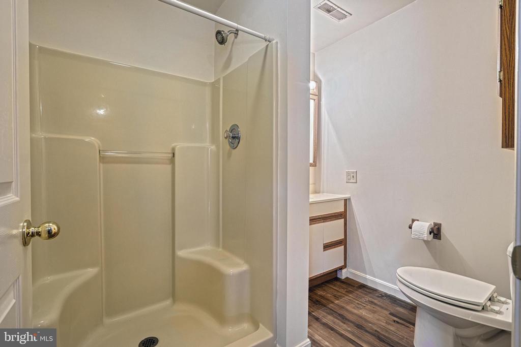 Bathroom with a cream tub-shower enclosure, white toilet, small vanity, and dark wood-look flooring.