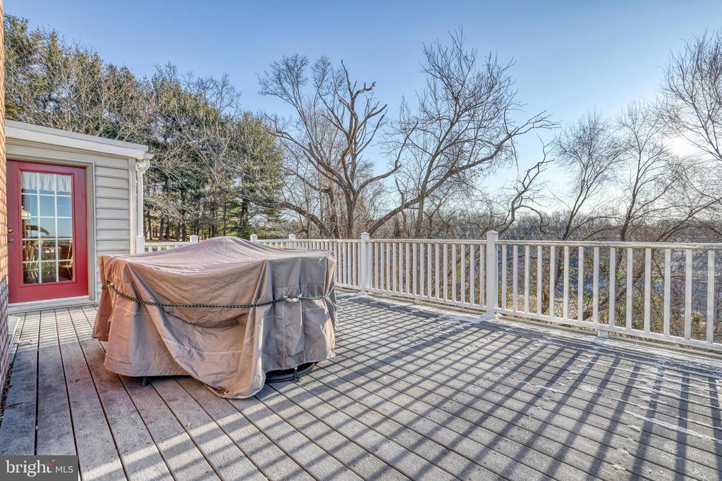 Elevated deck with a covered hot tub, white railing, and a wooded view.