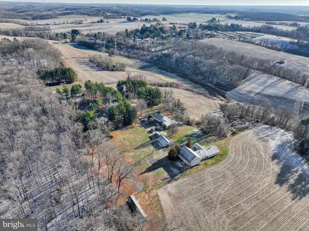 Rural property with a house and outbuildings amid winter fields and woodland.