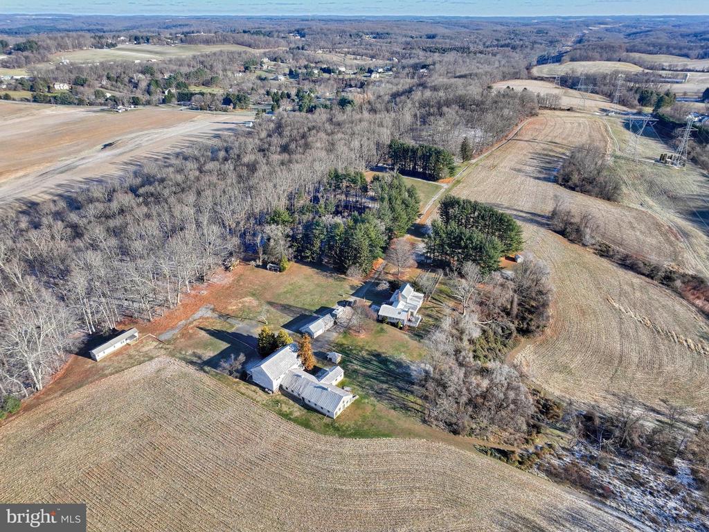 Rural property with several buildings, open fields, and wooded areas viewed from above.
