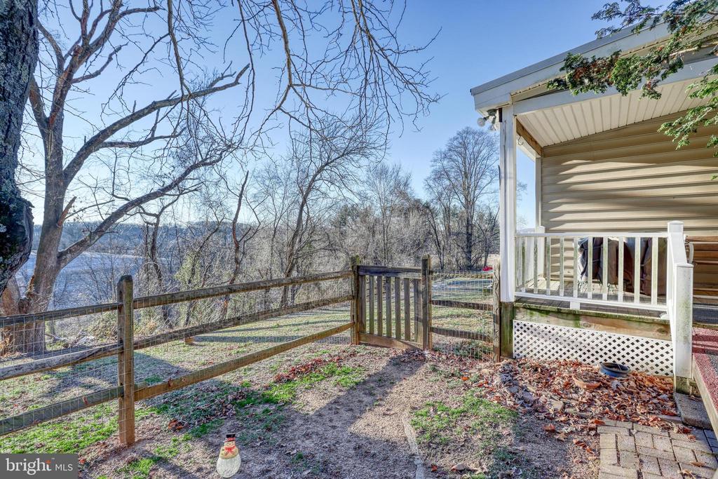 Fenced backyard with a porch and patio, bare trees, and a view of water.