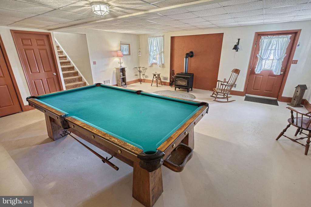 Recreation room with a large green-felt pool table, wood-burning stove, and rocking chair.