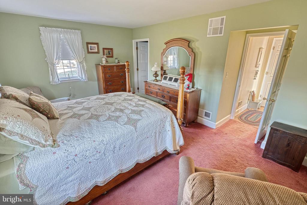 Bedroom with a white quilted bed, wooden dressers, pale green walls, and pink carpet.