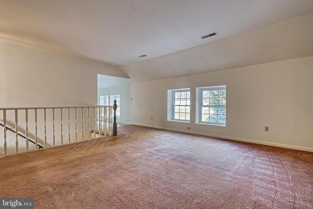 Empty carpeted upper-level room with two windows and a railing overlooking the stairs.
