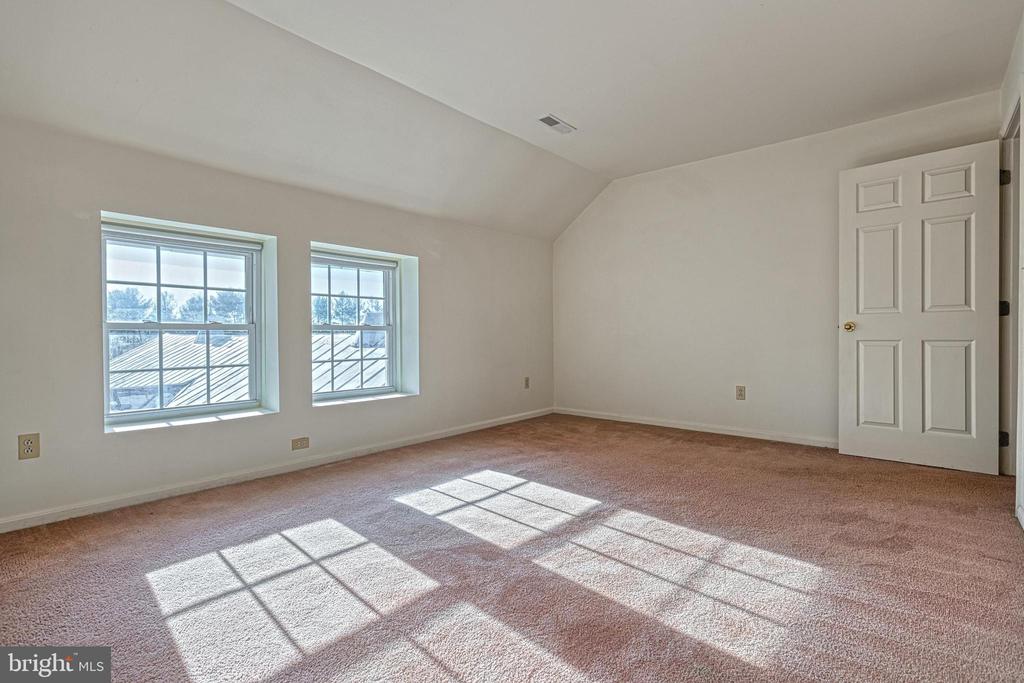 Empty bedroom with beige carpet and sunlight streaming through two windows.