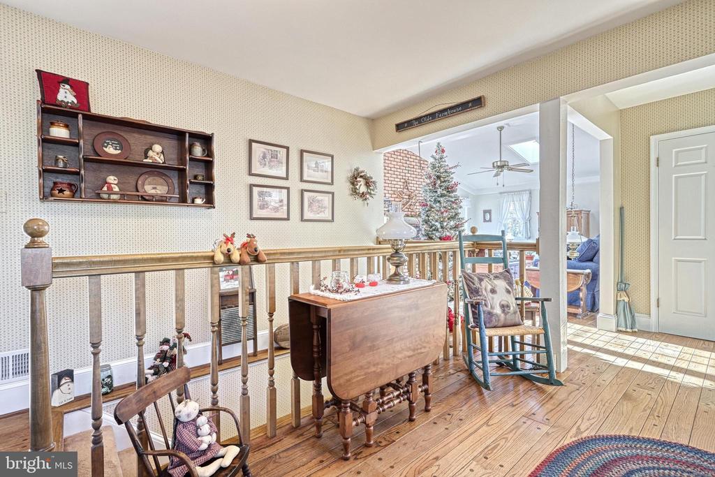 Furnished upstairs landing with hardwood floors, a wooden railing, rocking chairs, and a Christmas tree in the adjoining room.