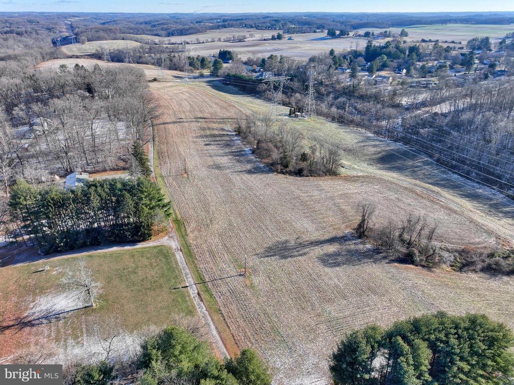 Aerial view of open fields bordered by woods, crossed by high-voltage power lines.