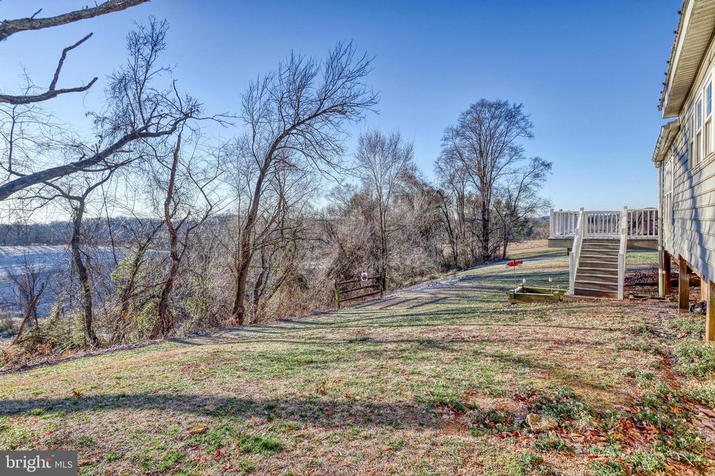 Sloping backyard beside a raised deck, with leafless trees and water beyond.