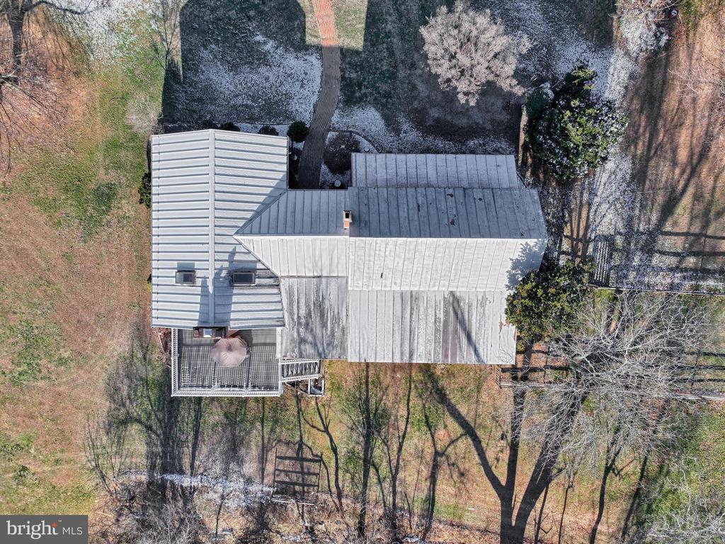 Aerial view of a metal-roofed house with a screened porch and patchy snow in the yard.