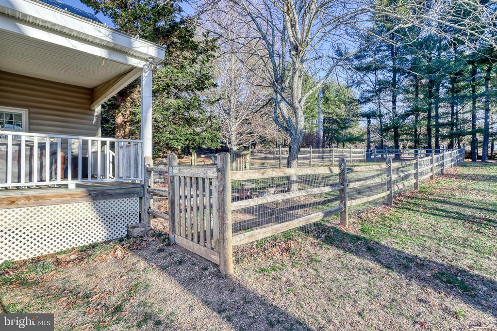 Fenced yard beside a covered porch, with a wooden gate and mature trees.