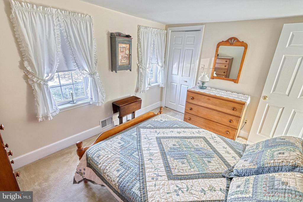 Bedroom with a blue-and-white quilted bed, curtained windows, and a wooden dresser with mirror.