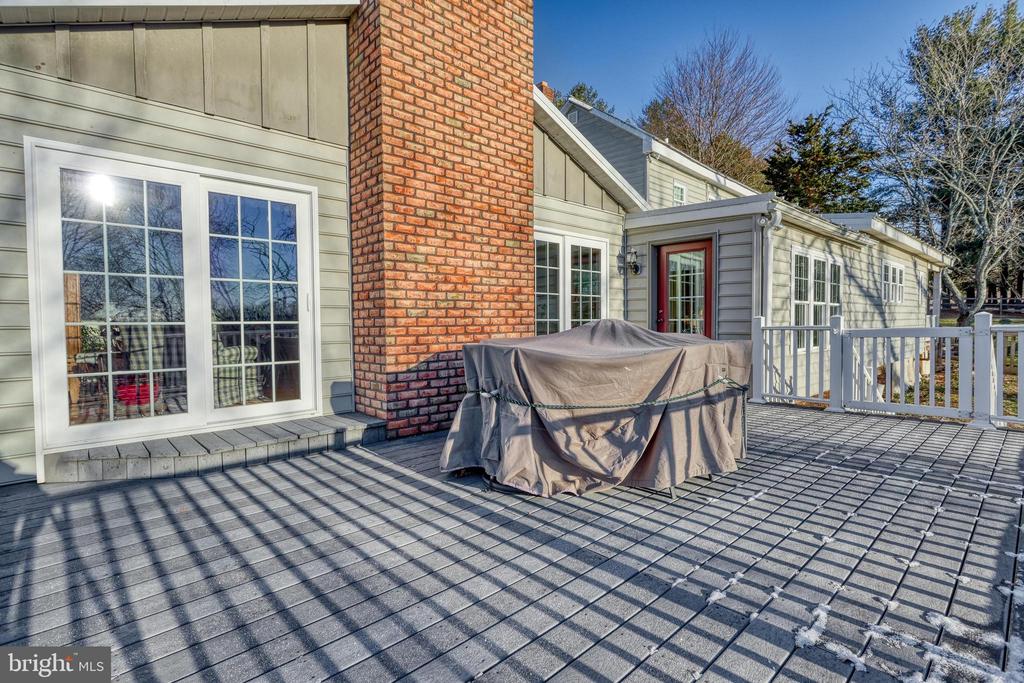 Rear deck with gray decking, white railings, a brick chimney, and covered outdoor furniture.