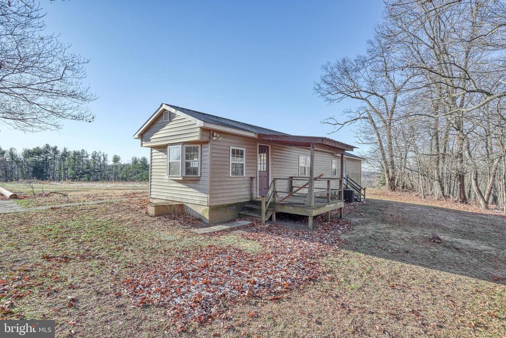 Small-sided house with a covered porch and bay window on an open, wooded lot.