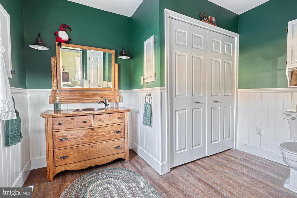 Bathroom with a wooden vanity and mirror, green walls, white wainscoting, and a large paneled door.