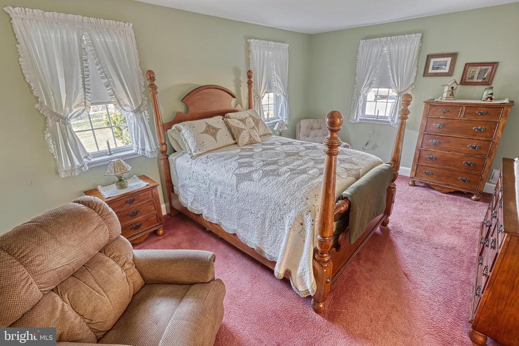 Bedroom with a wooden four-poster bed, rose-colored carpet, and sage-green walls.