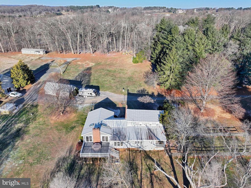 Aerial view of a home with a rear deck, broad lawn, wooded boundary, and RV in the driveway.