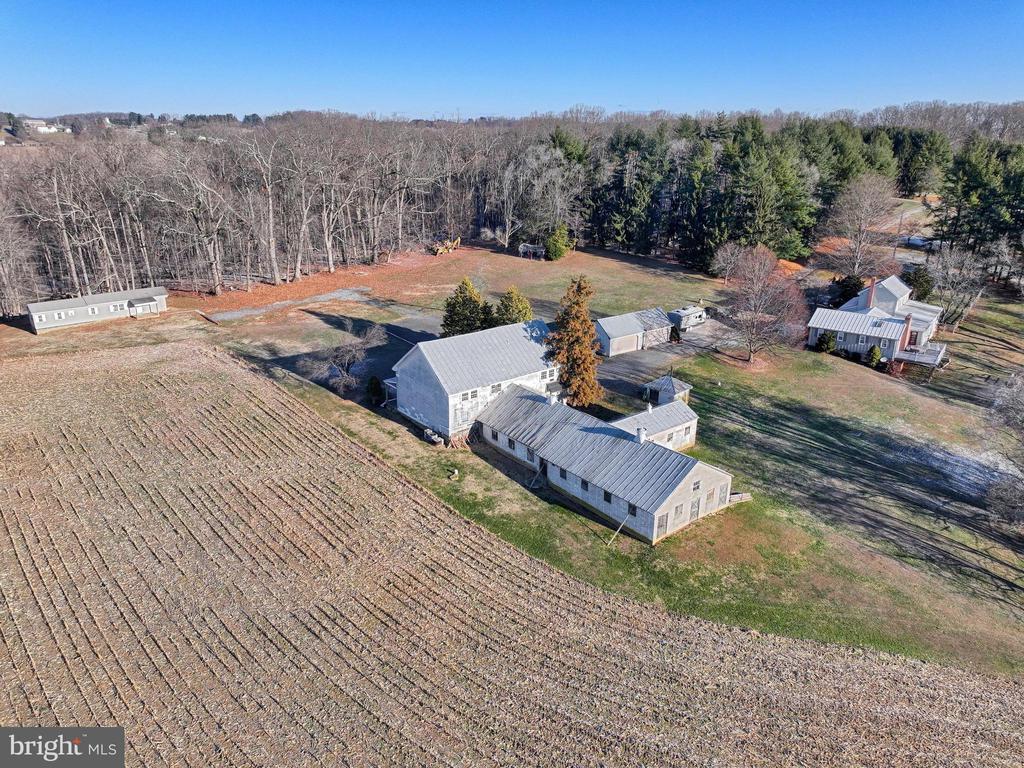 Aerial view of rural property with long outbuildings, cultivated field, and surrounding woodland.