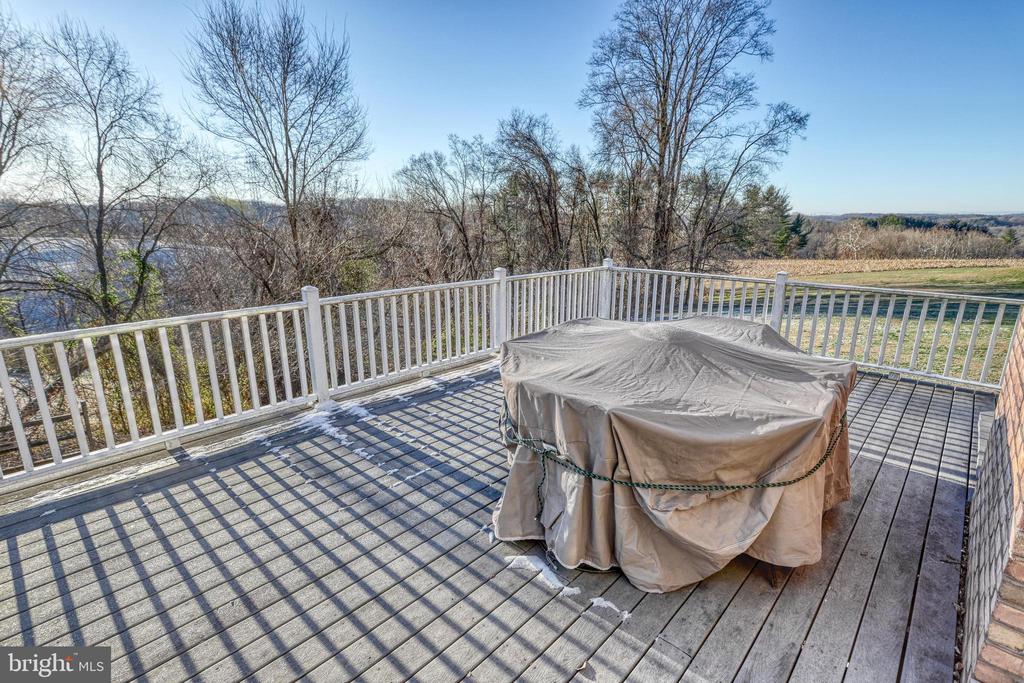 Wood deck with white railings and a covered grill overlooking water and leafless trees.